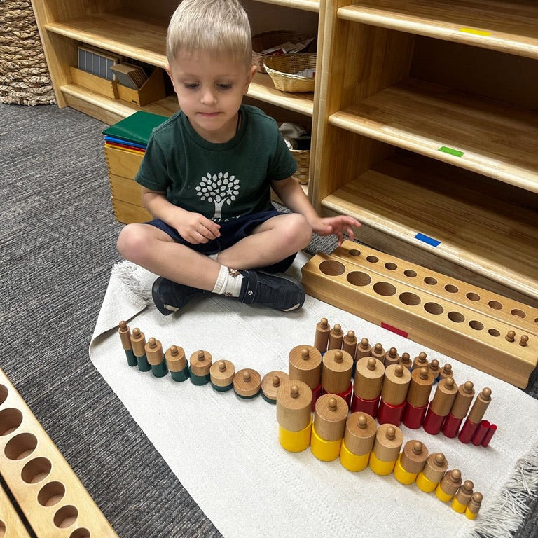 Child playing with wooden educational toys on a rug in a classroom setting.